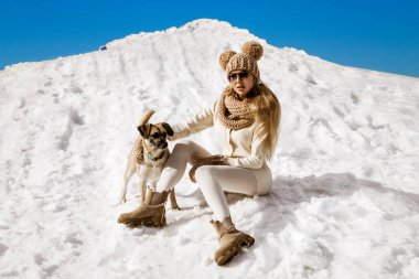 Güzel, şık bir kadın, kış manzarasında dağlarda köpeğiyle karda oynuyor. Kış tatili.