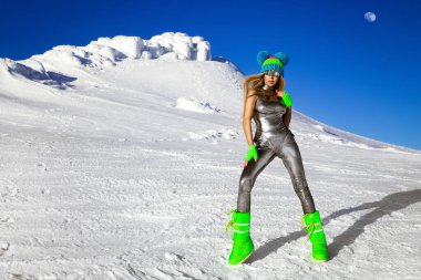 Sexy woman in silver cosmic outfit silver and winter boots is posing in the mountains. Female model in glamour silver jumpsuit in winter scenery. clipart