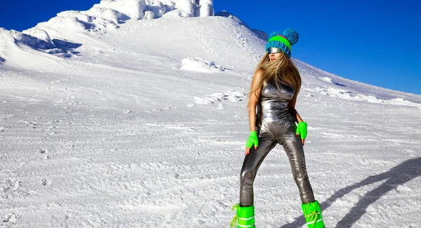 Sexy woman in silver cosmic outfit silver and winter boots is posing in the mountains. Female model in glamour silver jumpsuit in winter scenery.