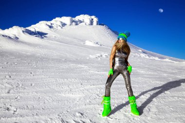 Gümüş kozmik kıyafetli, gümüş rengi çizmeli seksi kadın dağlarda poz veriyor. Kış manzarasında gümüş tulumlu bir kadın model..