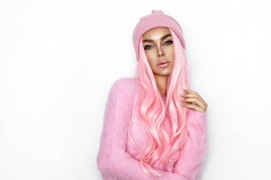 Güzel genç kız beyaz arka planda örülmüş şapka ve pembe kazak giyiyor. Kış modası.