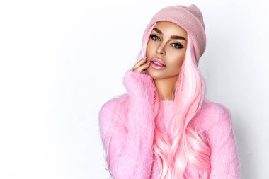 Güzel genç kız beyaz arka planda örülmüş şapka ve pembe kazak giyiyor. Kış modası.