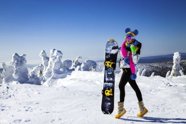 Kız snowboardcu kayak merkezinin tadını çıkarıyor. Kış kıyafetli güzel bir kadın dağlarda snowboard ile poz veriyor. Kış sporları. Snowboard..