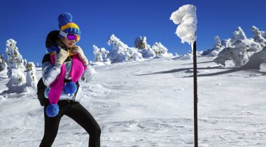 Winter fashion. Beautiful girl is wearing jacket, ski goggles and colorful winter hat and is posing on mountains background. Szrenica, Poland. Mountain travel.