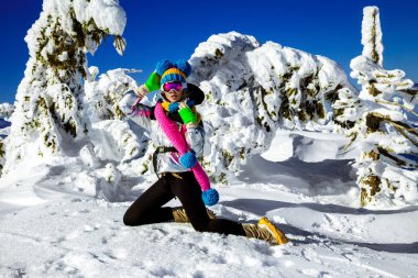 Winter fashion. Beautiful girl is wearing jacket, ski goggles and colorful winter hat and is posing on mountains background. Szrenica, Poland. Mountain travel.