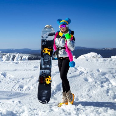 Kız snowboardcu kayak merkezinin tadını çıkarıyor. Kış kıyafetli güzel bir kadın dağlarda snowboard ile poz veriyor. Kış sporları. Snowboard..