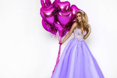 Harika uzun elbiseli güzel bir kadın pembe balonlar tutuyor ve beyaz arka planda poz veriyor. Elbise giymiş zarif bir kadın manken. Zarafet. Cazibe.