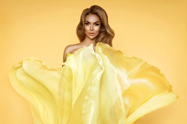 黄色のなびくドレスのファッション女性 グラマー風に乗って飛んでロングシルク生地で踊るモデル — ストック写真