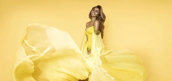 黄色のなびくドレスのファッション女性 グラマーモデルはロングシルク生地で風に乗って飛んでポーズをとっています — ストック写真