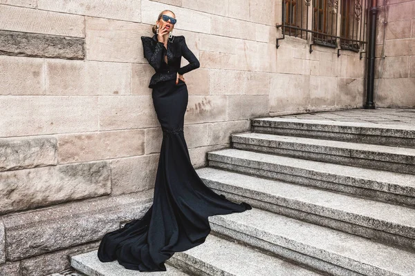 雅致的豪华晚礼服 穿着黑色长袍礼服的迷人 优雅的女人正站在城外 女模特穿着惊人的长裙 户外射击 服装设计 — 图库照片