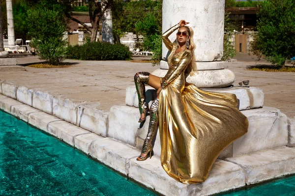 長い黄金の夜のドレスのエレガントな女性はトルコの高級リゾート地で屋外をポーズしています 驚くほど長いドレスの女性モデル ヴォーグ クチュール — ストック写真