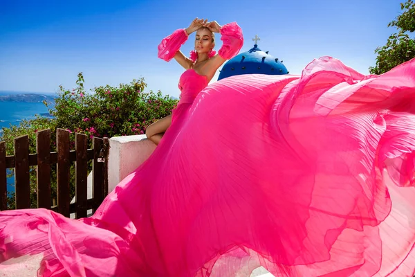 ピンクの長いなびくドレスのグラマーでスタイリッシュなエレガントな女性は サントリーニ島の高級リゾートで屋外をポーズしています 驚くほど長いドレスの女性モデル ヴォーグ クチュール — ストック写真