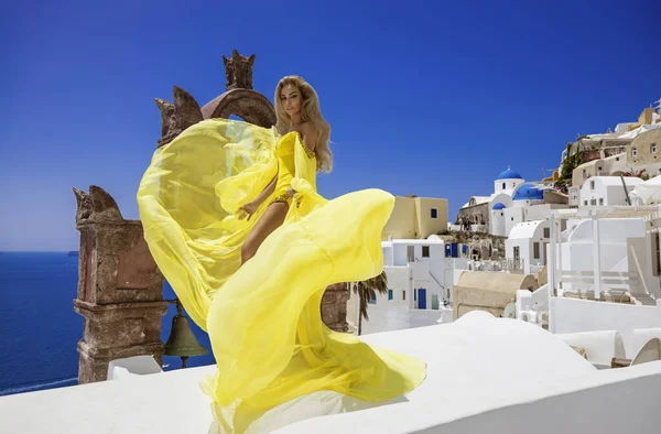 グラマー 黄色の長い飛行服のスタイリッシュなエレガントな女性はサントリーニ島のFiraでポーズをとっています — ストック写真