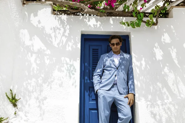 Elegant handsome man in blue suit is posing near in Fira in Santorini. Groom. Engagement and wedding in Santorini island of Greece.