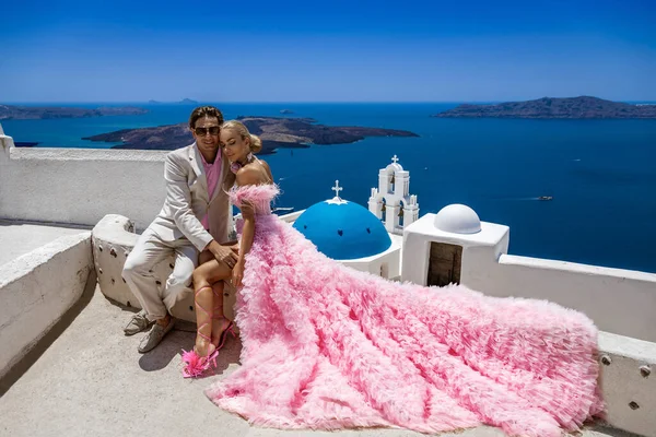Summer love. Beautiful happy young couple in wedding clothes is posing near Church of the Three Bells in Fira in Santorini. Engagements and wedding in Santorini island of Greece.