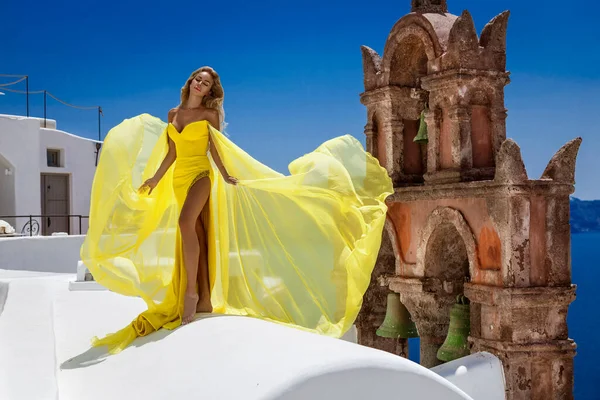 グラマー 黄色の長い飛行服のスタイリッシュなエレガントな女性はサントリーニ島のFiraでポーズをとっています — ストック写真
