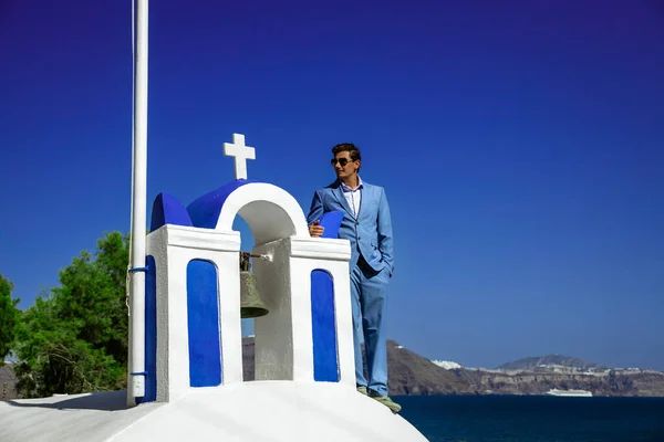 青いスーツのエレガントなハンサムグロムは オイアのサントリーニ教会の近くにポーズしています ギリシャのサントリーニ島での婚約と結婚式 ギリシャの結婚式 — ストック写真