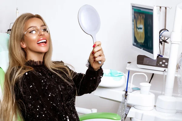 Beautiful happy woman sitting in the dentist chair and enjoying her new smile. Porcelain veneers.