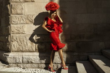 Cazibeli, zarif bir kadın gül çiçeği biçiminde kırmızı bir elbise giyiyor ve yaz günü açık havada poz veriyor..
