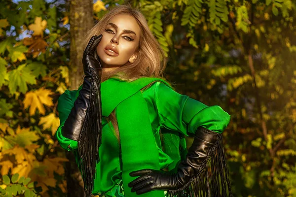 Beautiful woman wearing a green coat and elegant clothing is posing outdoors on a sunny autumn day.
