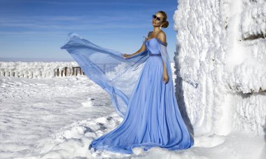 Mavi kanat çırpan uzun elbiseler giyen zarif bir kadın ve güneşli bir günde dağlarda poz veriyor. Kar Kraliçesi.