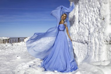 Mavi kanat çırpan uzun elbiseler giyen zarif bir kadın ve güneşli bir günde dağlarda poz veriyor. Kar Kraliçesi.