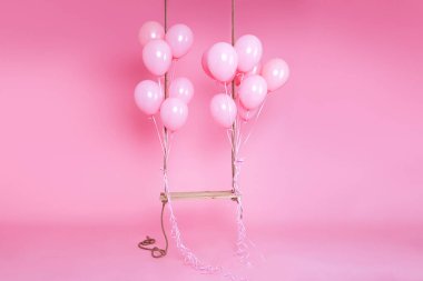 Stüdyoda pembe arka planda pembe balonlarla süslenmiş romantik bir salıncak. Doğum günü ve düğün konsepti. Tatil ve etkinlikler için dekor.