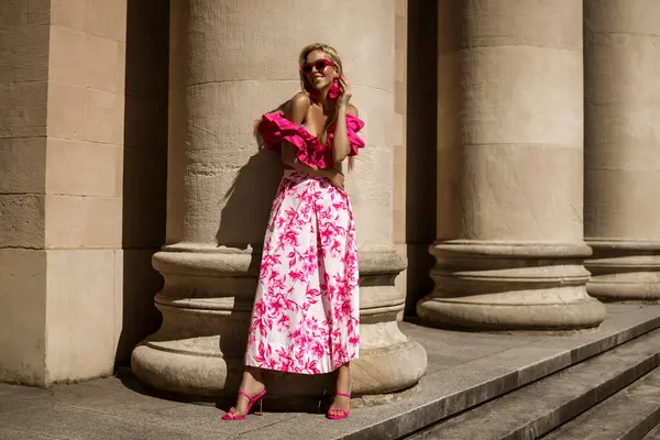 ピンクの花のドレスとセクシーなハイヒールのエレガントでスタイリッシュな女性は 晴れた夏の日に街を感動的に歩いています アウトドアシュート ストック写真