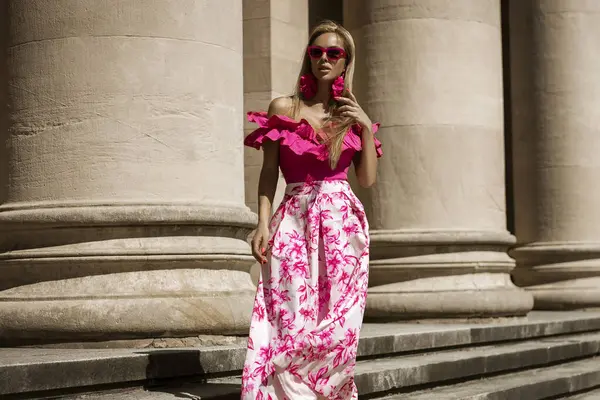 ピンクの花のドレスとセクシーなハイヒールのエレガントでスタイリッシュな女性は 晴れた夏の日に街を感動的に歩いています アウトドアシュート ストック画像