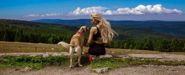 Gülümseyen dişi köpek sahibi yaz mevsiminde birlikte yürüdükleri sırada dağ nehri şelalesinde dinlenen arkadaşına sarılıyor. İnsan ve evcil hayvanlar ya da doğa konsepti imajı.