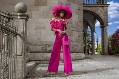 Bahar yaz modası. Yüksek model. Cazibeli, zarif, pembe tulumlu ve büyük şapkalı kadın. Şehirde şık görünümlü bir kadın model. Açık hava çekimi..