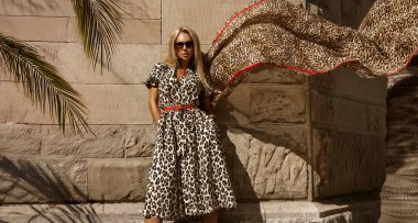 Zarif, şık, leopar desenli bir elbise giyen sarışın manken yaz günü şehrimizde şehvetle yürüyor. Açık hava çekimi..