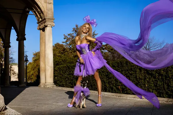 Yazlık elbisesi ve yüksek topuklu ayakkabıları olan zarif sarışın bir kadın şehirde küçük bir köpekle baştan çıkarıcı bir şekilde yürüyor..