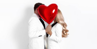 Beyaz arka planda birbirine aşık mutlu güzel bir çift ve ellerinde kırmızı sevgililer günü balonları var. Sevgililer Günü için romantik fotoğraf