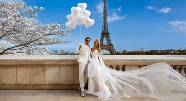 Zarif beyaz giysiler içinde güzel romantik bir çift Paris 'te Eyfel Kulesi' nin yanında sevgililer günü balonları tutuyor. Sevgililer Günü