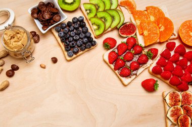 A vibrant assortment of fruit-topped toasts with peanut butter and chocolate spread, featuring strawberries, raspberries, blueberries, kiwi, figs, and oranges on a wooden background. clipart