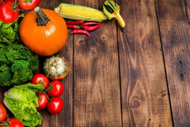 Kabak, mısır, kırmızı biber, domates ve ahşap bir arka planda taze yeşillikler içeren canlı bir sonbahar hasat düzenlemesi. Mevsimlik mutfak ilhamı için mükemmel..