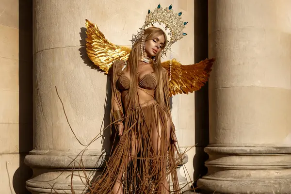 Lüks makrome elbise, altın kanatlar ve tanrıça saç bandı giymiş güzel seksi sarışın manken yaz günü şehirde şehvetle poz veriyor. Yaz Modeli.