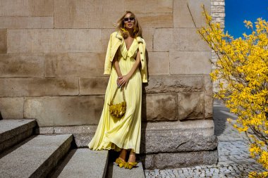 Akan sarı Maxi elbiseli zarif kadın güneşli bir yaz gününde şehirde sarı fındık çiçeklerinin yanında poz verir..