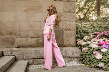 Zarif pembe takım elbiseli ve çiçekli gömlekli güzel bir kadın güneşli bir yaz gününde şehrimizde şehvetle dolaşıyor. Lüks yaz modası