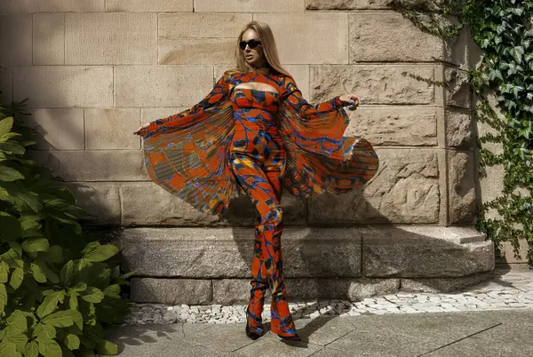 Kelebek kollarıyla renkli tulum giymiş güzel bir manken güneşli bir yaz gününde şehrimizde şehvetli pozlar veriyor. Açık havada fotoşop. Kelebek kadın.