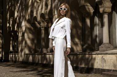 Güzel ve zarif bir kadın. Beyaz, şık bir takım elbise giymiş. Şehrimizde şehvetli bir şekilde dolaşıyor. Zarafet. İş kadını bakışı.