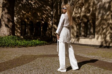 Güneşli bir yaz gününde beyaz, modaya uygun keten kıyafetler giyen zarif bir kadın manken şehrimizde şehvetle dolaşıyor. Zarafet. Yaz modası