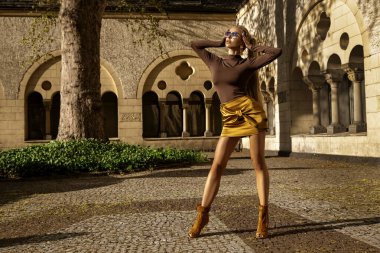 Şık yaz elbisesi içinde uzun sarı saçlı güzel kadın manken güneşli bir yaz gününde şehirde şehvetli pozlar veriyor. Yaz Moda..