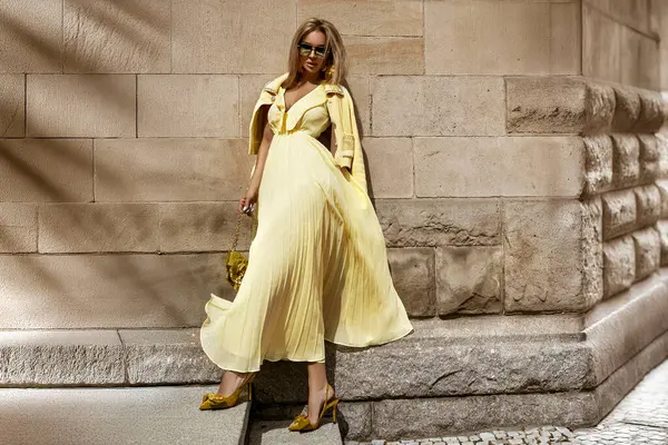 Güneşli bir yaz gününde şehirde dalgalı sarı maksi elbiseli bir manken poz verir..