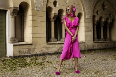 Pembe, sarı saçlı, uzun ve çekici yaz elbisesi giyen zarif kadın manken güneşli bir yaz gününde şehrimizde şehvetli pozlar veriyor. Yaz Moda..