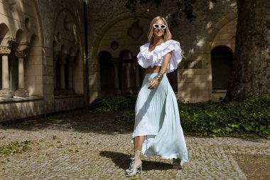 Uzun sarı saçlı, mavi etekli ve dalgalı bluzlu zarif manken güneşli bir yaz gününde şehrimizde şehvetli pozlar veriyor. Yaz modası.