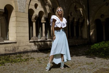 Uzun sarı saçlı, mavi etekli ve dalgalı bluzlu zarif manken güneşli bir yaz gününde şehrimizde şehvetli pozlar veriyor. Yaz modası.