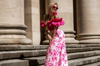 Pembe çiçekli yaz eteği ve şık fırfırlı bluzla şık, şık bir model güneşli bir yaz gününde şehrimizde şehvetli bir şekilde dolaşıyor. Açık havada fotoşop.