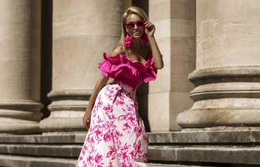 Pembe çiçekli yaz eteği ve şık fırfırlı bluzla şık, şık bir model güneşli bir yaz gününde şehrimizde şehvetli bir şekilde dolaşıyor. Açık havada fotoşop.